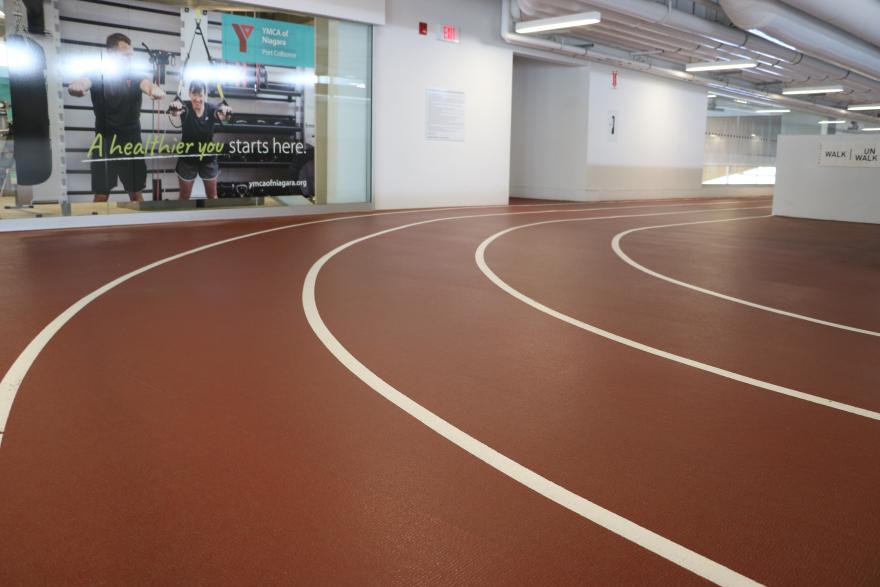 Indoor running track with a smooth, maroon surface and white lines, leading to a glass wall.