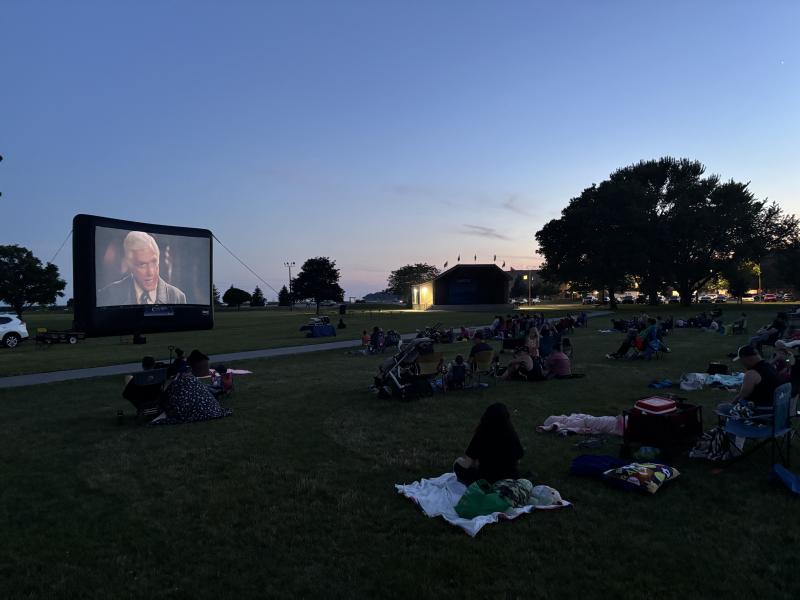 Outdoor movie screening in a park at dusk, with several people watching on blankets.