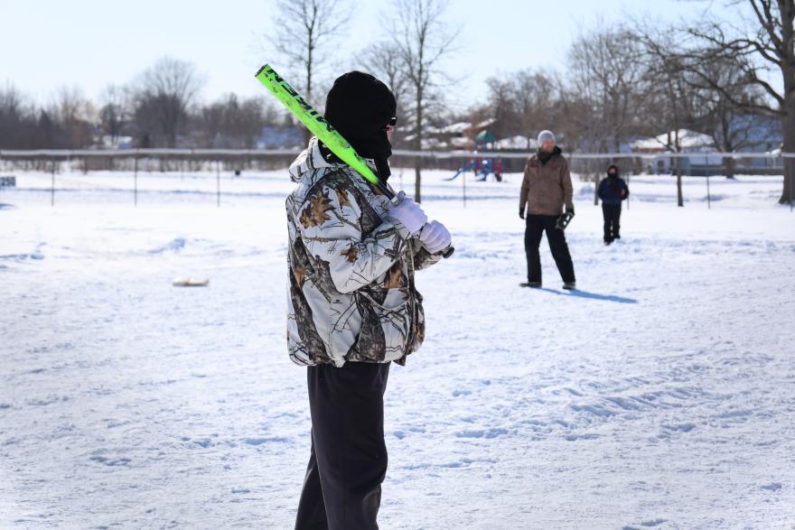 Person holding a green bat, standing in a snowy field with others in the background.