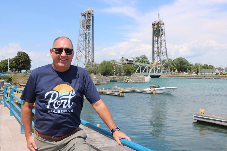 Person in a blue shirt standing by a river with lift bridges and boats in the background.