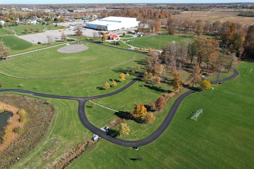 Aerial view of a park with winding paths, trees showing autumn colours, and a large building nearby.