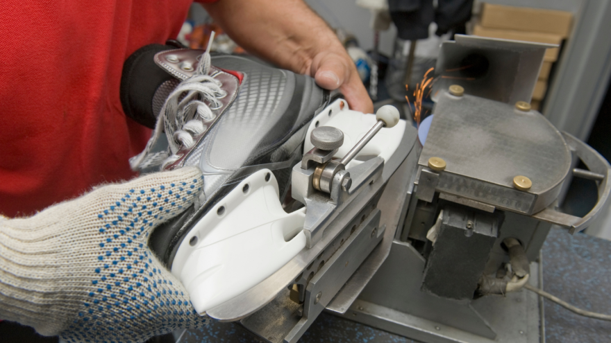 A hand holding a skate being sharpened by a machine in a workshop.